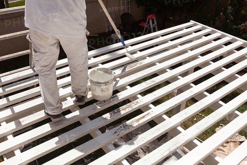 Professional painter rolling white paint onto the top of A home patio cover