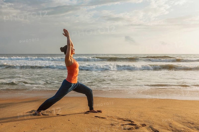 Woman doing Hatha yoga asana Virabhadrasana 1 Warrior Pose outdoors on ocean beach on sunset. Kerala