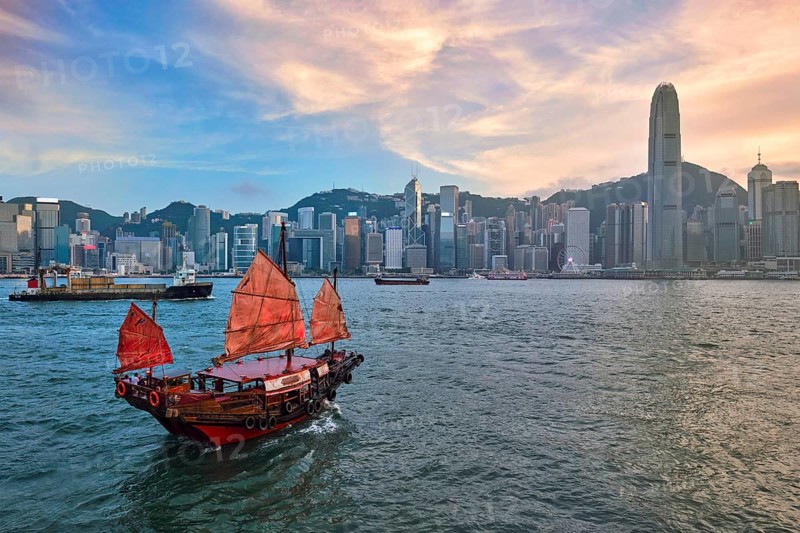 Hong Kong skyline cityscape downtown skyscrapers over Victoria Harbour in the evening with junk tourist ferry boat on sunset with dramatic sky. Hong Kong