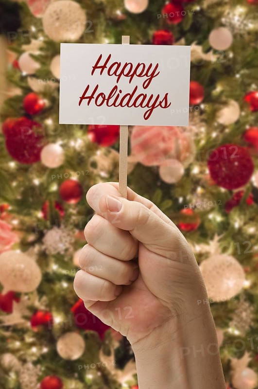Hand holding happy holidays card in front of decorated christmas tree