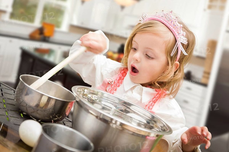 Cute baby girl playing cook with pots and pans in kitchen