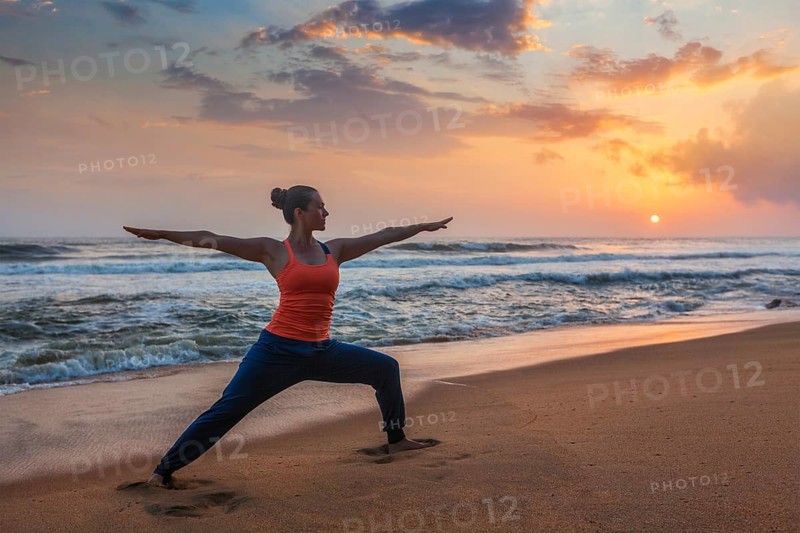 Woman doing Hatha yoga asana Virabhadrasana 1 Warrior Pose outdoors on ocean beach on sunset. Kerala