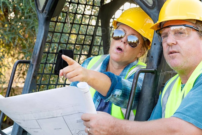 Male and female workers with technical blueprints talking at construction site