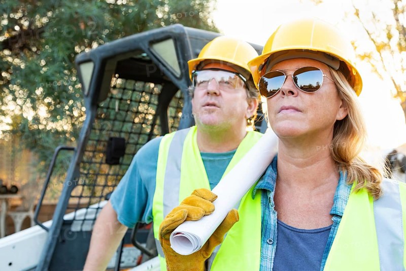 Male and female workers with technical blueprints at construction site