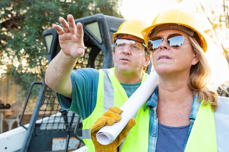 Male and female workers with technical blueprints talking at construction site