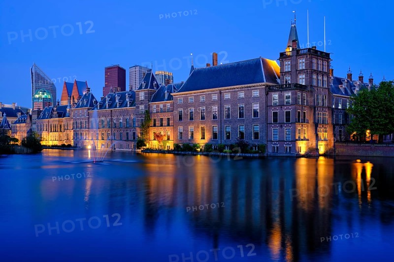 View of the Binnenhof House of Parliament and the Hofvijver lake with downtown skyscrapers in background illuminated in the evening. The Hague