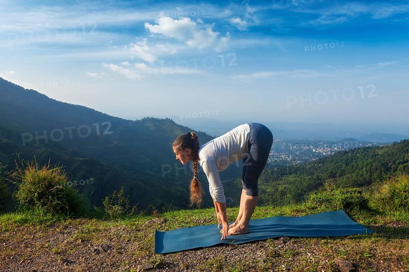 Young sporty fit woman doing yoga Sun salutation Surya Namaskar pose Uttanasana outdoors in mountains