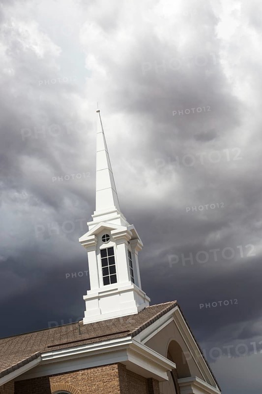 Church steeple tower below ominous stormy thunderstorm clouds
