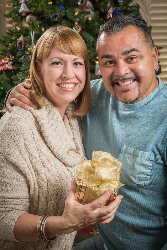 Happy young mixed-race couple with present near christmas tree