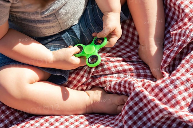 Baby boy sitting on picnic blanket playing with fidget spinner