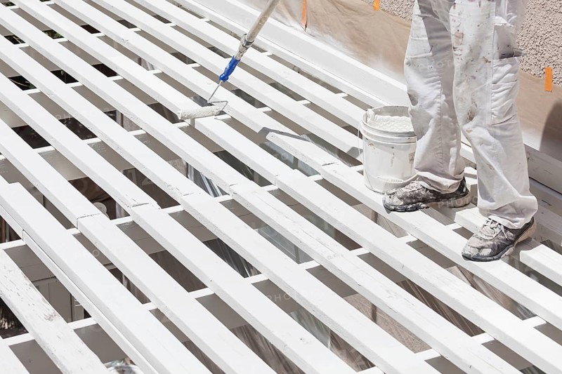 Professional painter rolling white paint onto the top of A home patio cover