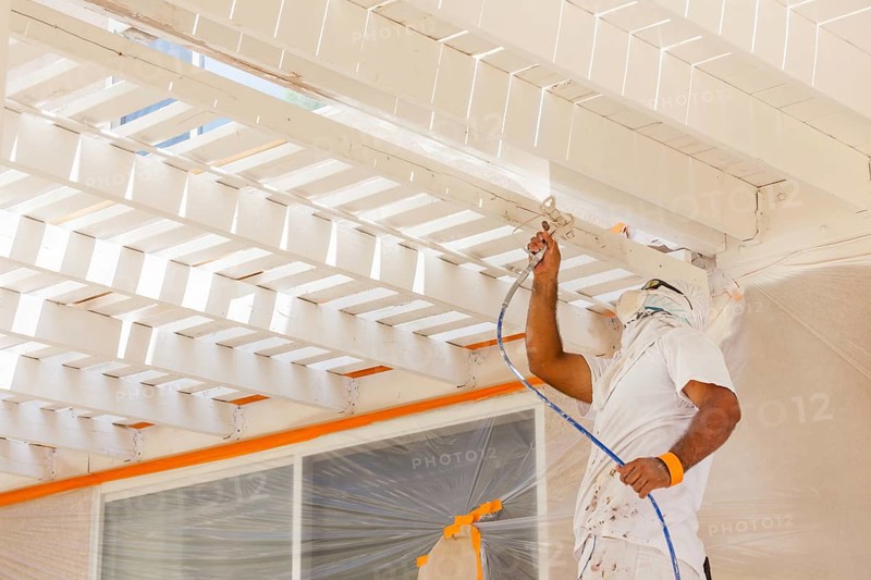 Professional house painter wearing facial protection spray painting deck of A home