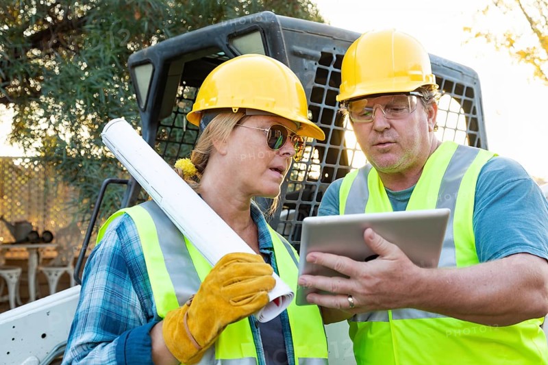 Male and female workers with technical blueprints and computer tablet talking at construction site
