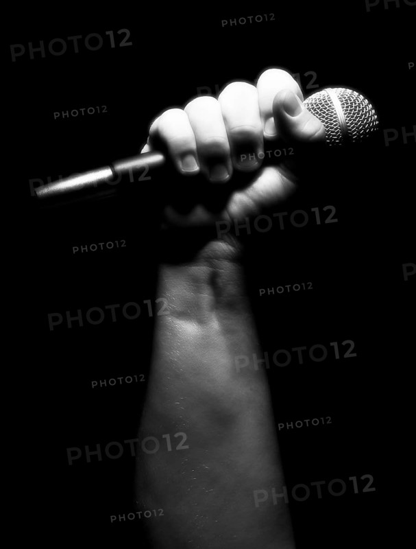 Gray scale vertical microphone clinched firmly in male fist on a black background