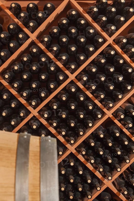 Several varietal wine bottles and barrel age inside dark cellar