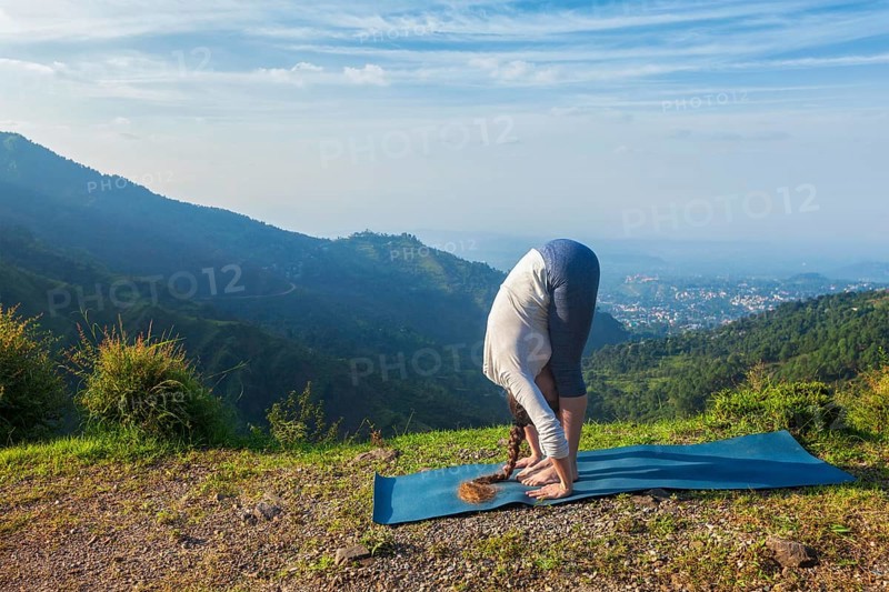 Young sporty fit woman doing yoga Sun salutation Surya Namaskar pose Uttanasana outdoors in mountains