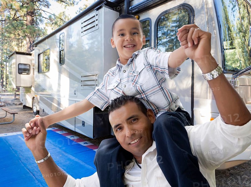 Happy hispanic father and son in front of their beautiful RV at the campground