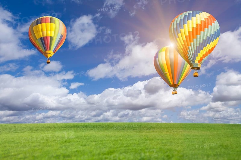 Two hot air balloons up in the beautiful blue sky with grass field below