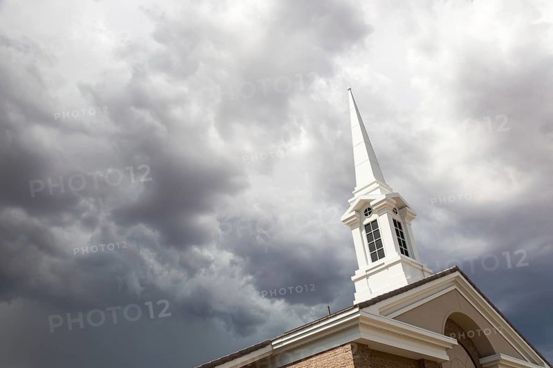 Church steeple tower below ominous stormy thunderstorm clouds