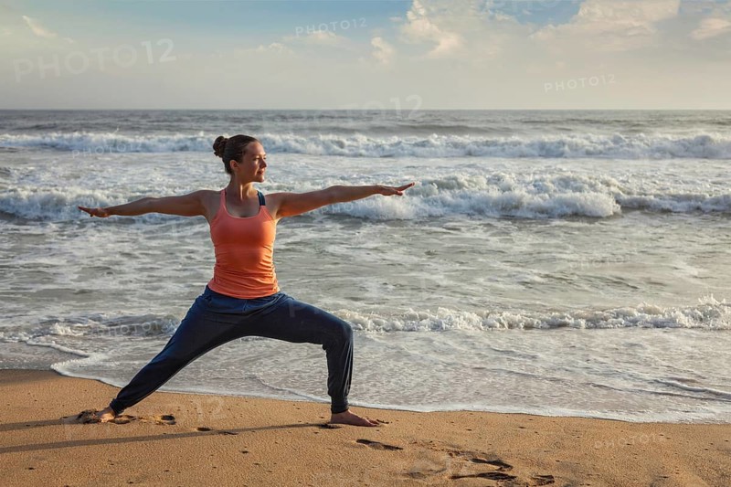 Woman doing Hatha yoga asana Virabhadrasana 1 Warrior Pose outdoors on ocean beach on sunset. Kerala