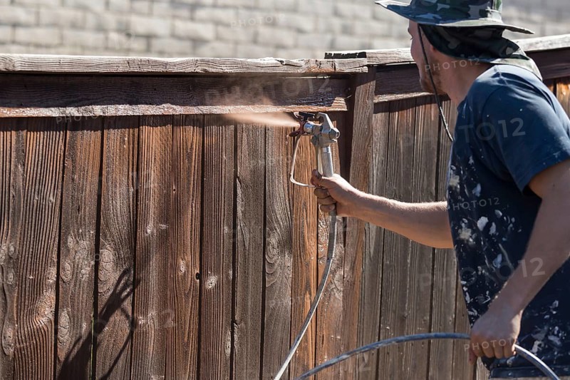 Professional painter spraying house yard fence with wood stain