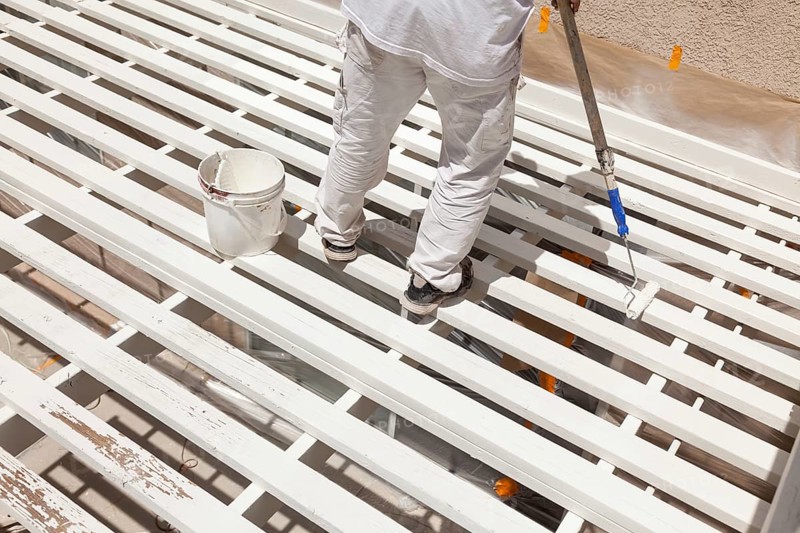 Professional painter rolling white paint onto the top of A home patio cover