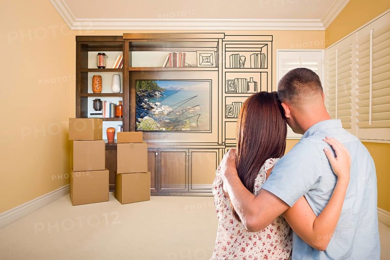 Young military couple looking at drawing of entertainment unit in room with moving boxes