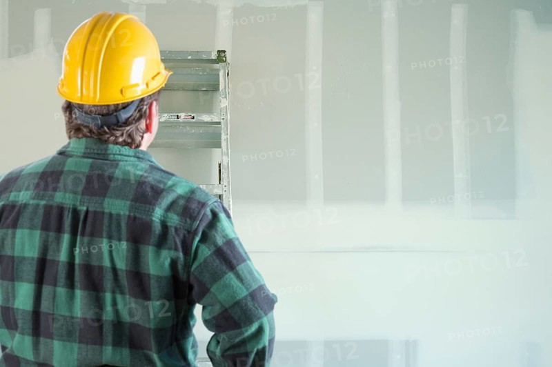 Contractor in hard hat looking at drywall