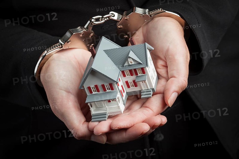 Woman in handcuffs holding small house against black