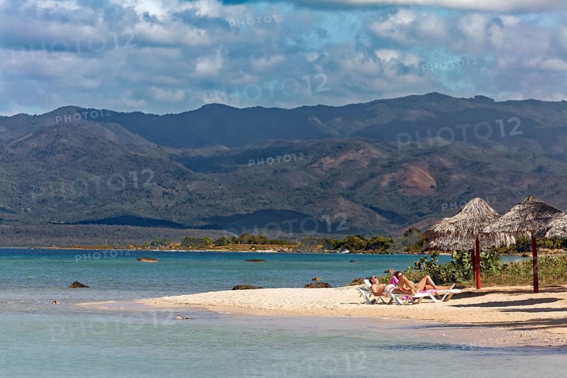 Couple lying on sun lounger on beach with parasol