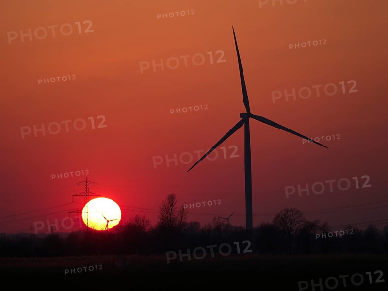Wind turbine and high-voltage line in front of the setting sun in Hamburg's Vier- und Marschlanden. Ochsenwerder