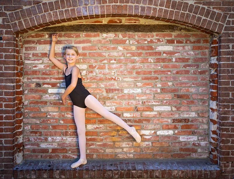 Cute caucasian ballerina girl posting against A brick wall