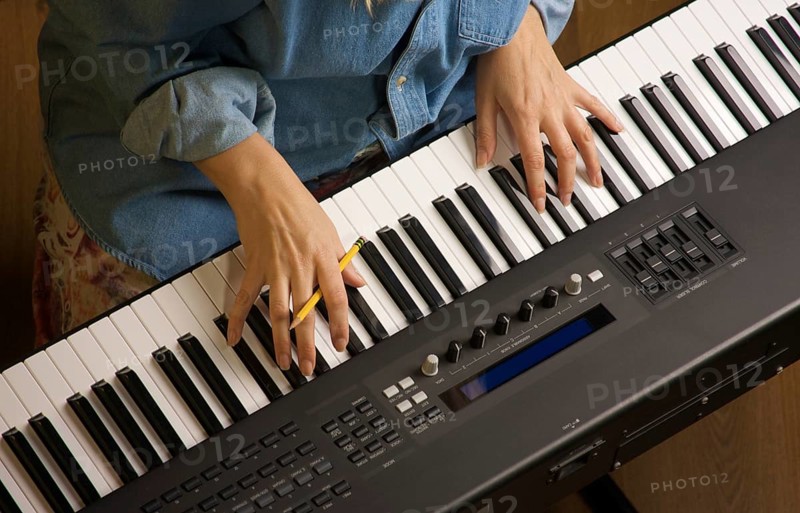 Woman's fingers with pencil on digital piano keys