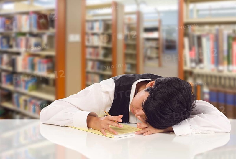 Young female mixed-race student stressed and frustrated in library with blank pad of paper