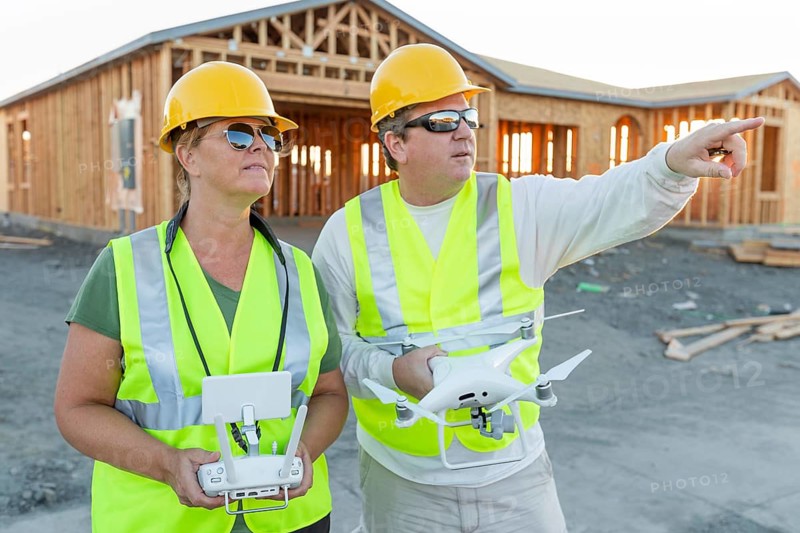 Workers with drone quadcopter inspecting photographs on controller at contruction site