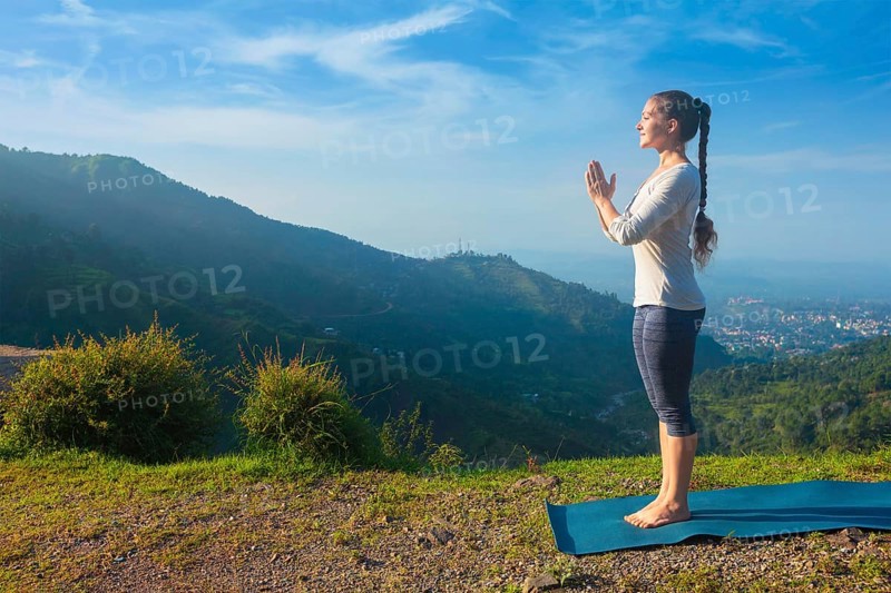 Woman doing Ashtanga Vinyasa Yoga asana Tadasana Samasthiti yoga posture in mountains in the morning