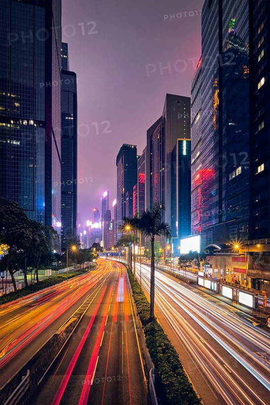 Street traffic in Hong Kong at night. Office skyscraper buildings and busy traffic on highway road with blurred cars light trails. Hong Kong