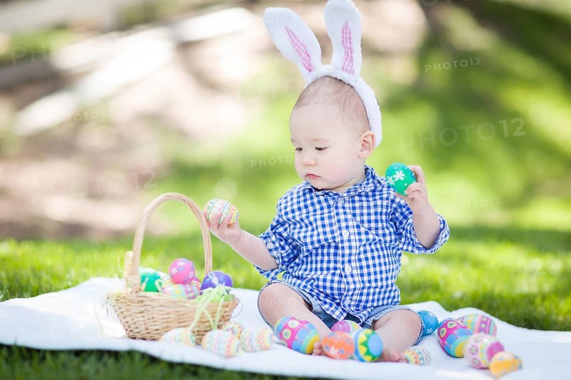 mixed-race chinese and caucasian baby boy outside wearing rabbit ears playing with easter eggs