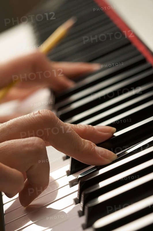 Woman's fingers with pencil on digital piano keys