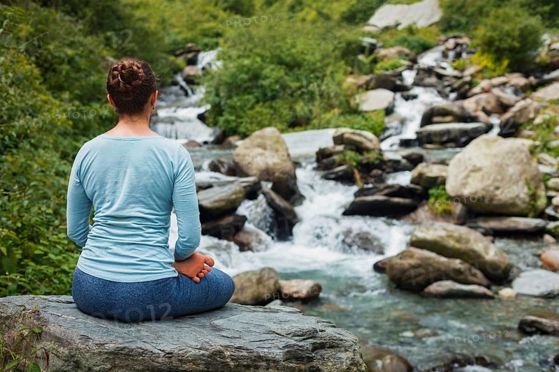 Woman in Hatha yoga asana Padmasana outdoors at tropical waterfall