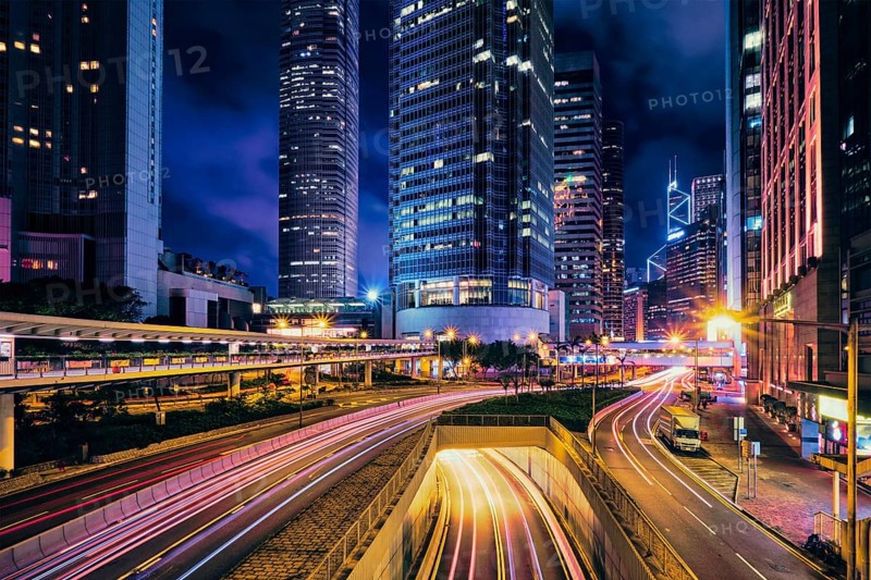 Street traffic in Hong Kong at night. Office skyscraper buildings and busy traffic on highway road with blurred cars light trails. Hong Kong