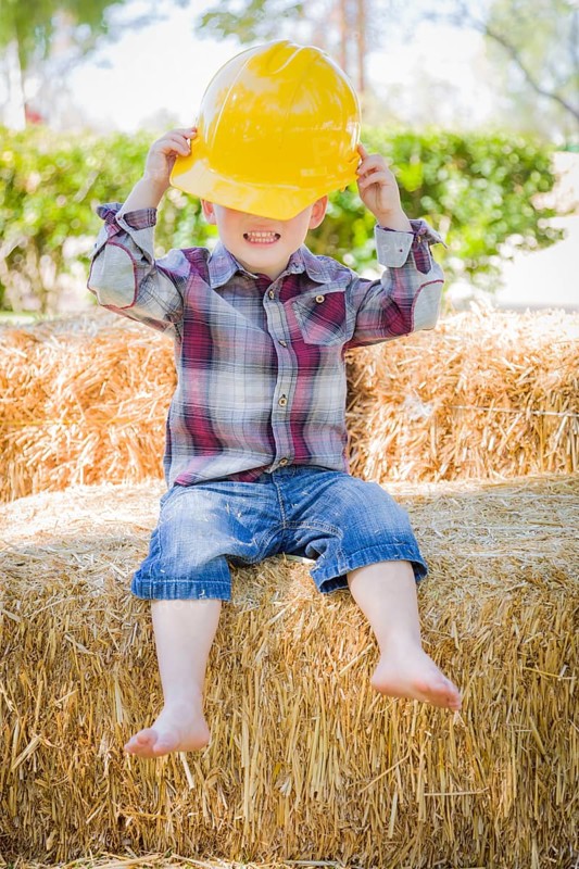 Cute young mixed-race boy laughing with hard hat outside sitting on hay bale