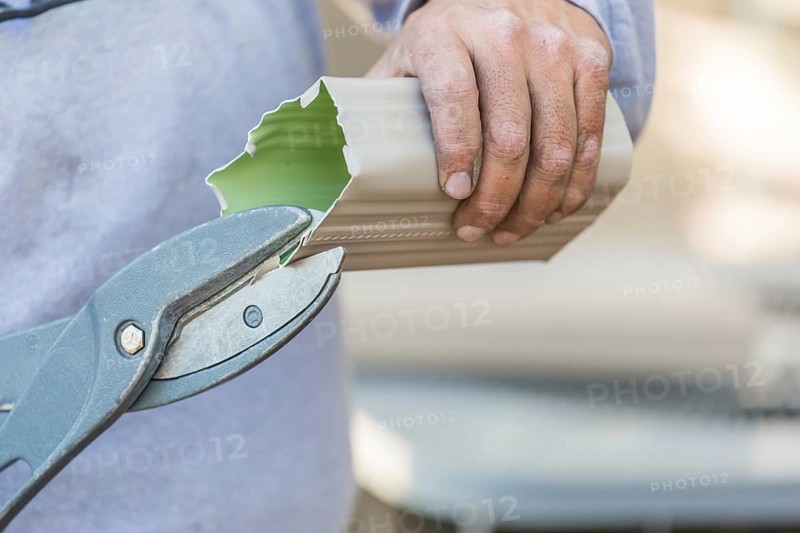 Worker cutting aluminum rain gutter with heavy shears