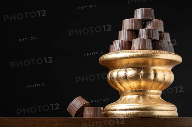 Stack of fine chocolates on golden pillar dish with dark background