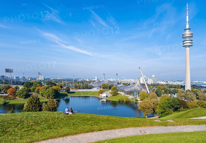Two people sitting in the park with Olympic lake and Olympic tower