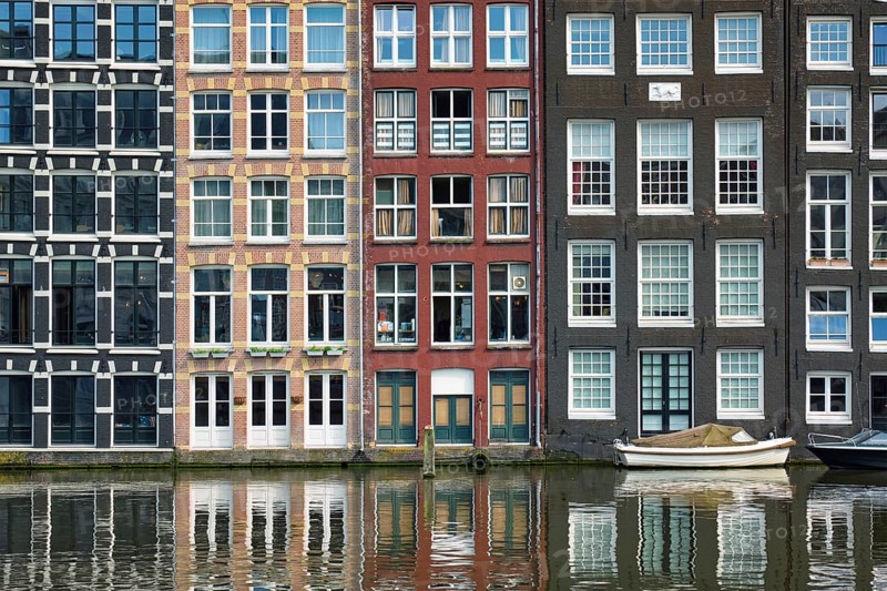 Row of typical houses and boat on Amsterdam canal Damrak with reflection. Amsterdam