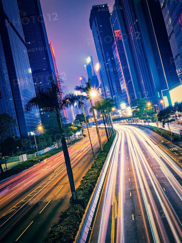 Street traffic in Hong Kong at night. Office skyscraper buildings and busy traffic on highway road with blurred cars light trails. Hong Kong