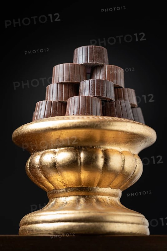 Stack of fine chocolates on golden pillar dish with dark background