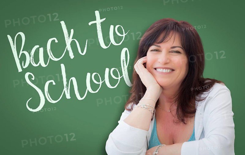 Back to school written on green chalkboard behind smiling middle aged woman