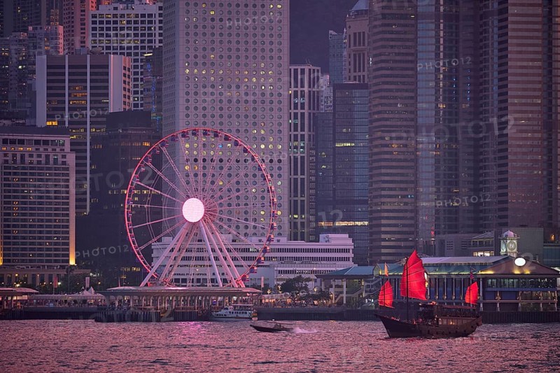 Tourist junk boat ferry with red sails and Hong Kong skyline cityscape downtown skyscrapers over Victoria Harbour in the evening. Hong Kong